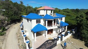 A two-story building with a blue roof and white walls, featuring a balcony and a staircase. - Homes for rent vacation rentals vacation rentals los Conuco de Villavaquez (Monte Plata)