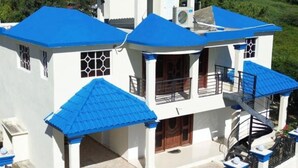 A two-story building with a blue roof and white walls, featuring a balcony and a staircase. - Homes for rent vacation rentals vacation rentals los Conuco de Villavaquez (Monte Plata)