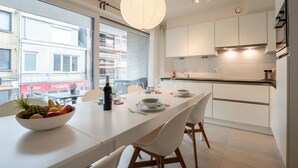 Una cocina moderna con armarios blancos, una mesa de comedor con sillas, un ventanal y una lámpara colgante.
