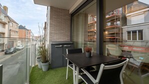 Un balcón con mesa y sillas, una planta en maceta y vistas a la calle y edificios.