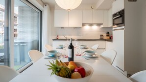Una cocina moderna con armarios blancos, una mesa de comedor con platos, vasos y un bol de fruta.