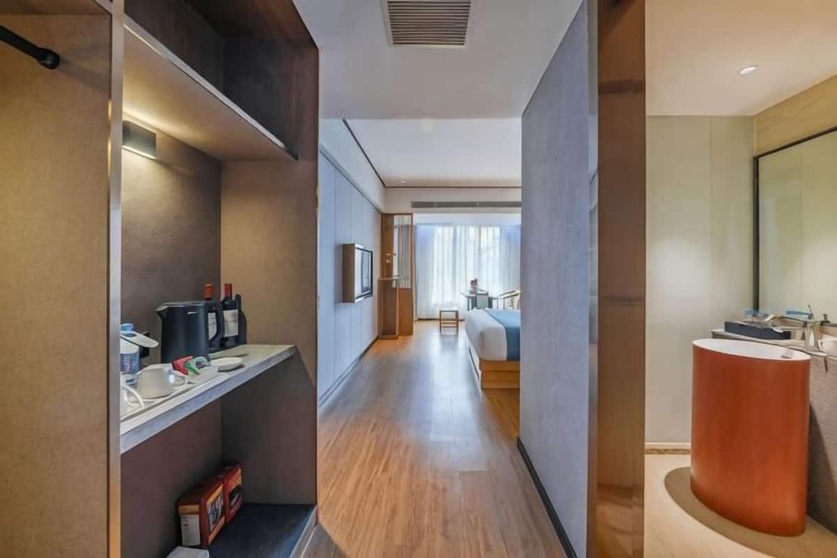 A hotel hallway with a wooden floor, a reception desk, a large mirror, and a modern bathroom with a curved sink.