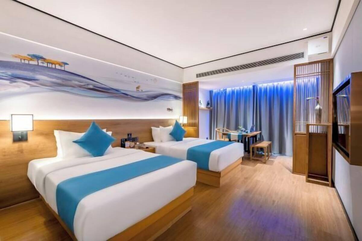 Une chambre d’hôtel avec deux lits, un bureau, une chaise, une télévision et une fresque murale.