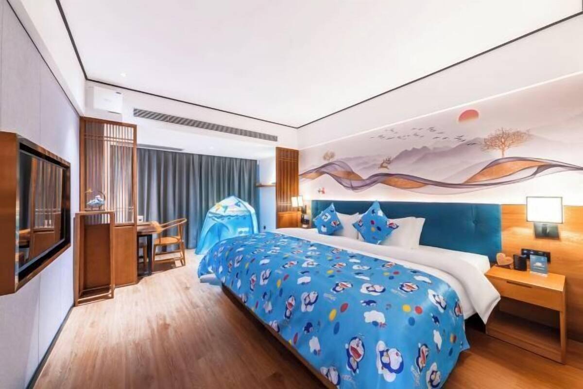 Une chambre d’hôtel comprenant un lit, un bureau, une chaise, une fenêtre et un mur orné d’une fresque.