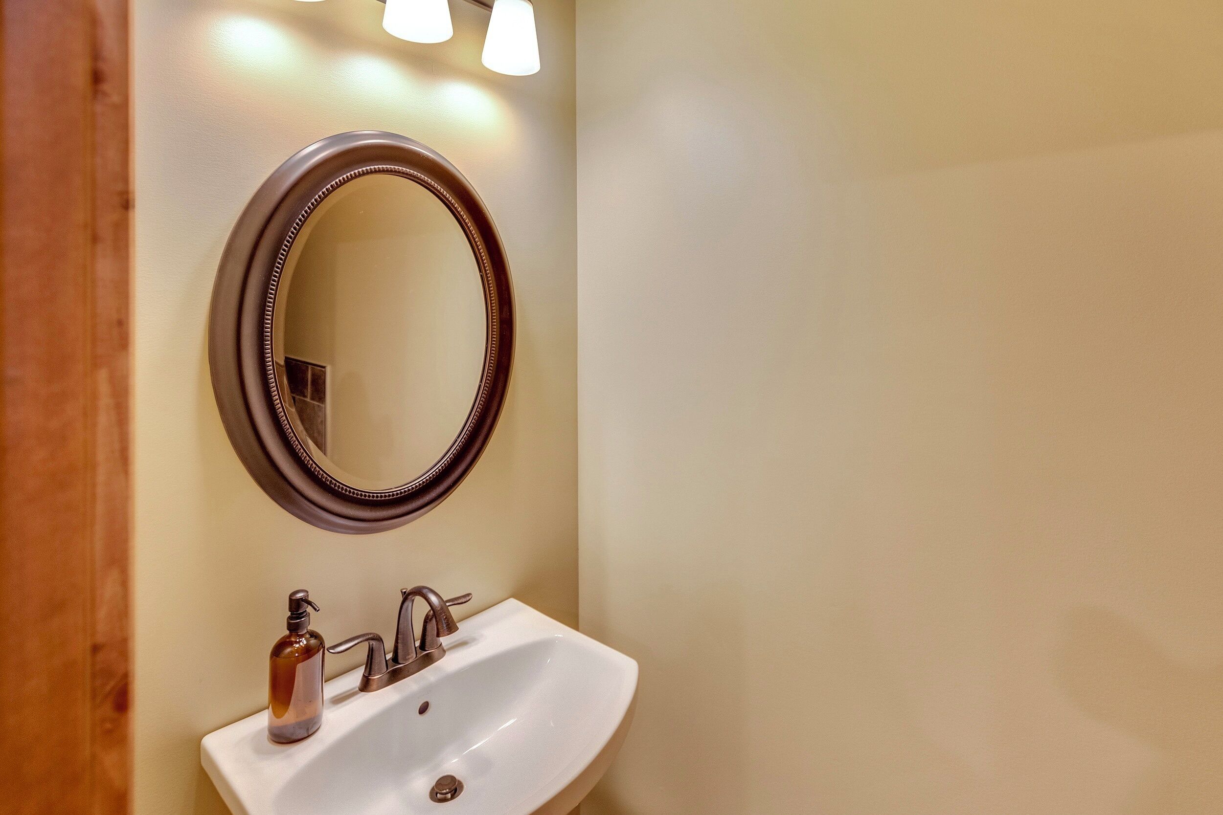 A bathroom with a white sink, a round mirror, and a soap dispenser.