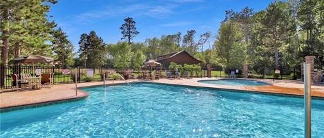 A clear swimming pool with lounge chairs and a covered seating area, surrounded by trees.