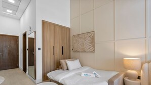 A hotel room with a bed, a bedside table, a lamp, a wardrobe, and a mirror. - Luxe Interior Studio in Pantheon Elysee 3 in JVC (Dubai)