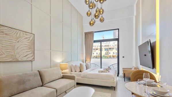 A modern living room with a sofa, a dining table set for two, and a TV mounted on the wall.