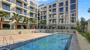Een modern gebouw met een zwembad, palmbomen en een heldere lucht.