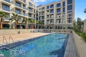 A modern building with a swimming pool, palm trees, and a clear sky.