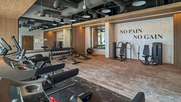 Een fitnessruimte met loopbanden, krachttrainingsapparatuur en een motiverende muur waarop staat: 'NO PAIN NO GAIN'.