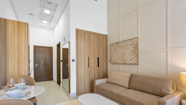 A modern hotel room with a dining area, a sofa, and a large mirror. - Luxe Interior Studio in Pantheon Elysee 3 in JVC (Dubai)
