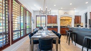 A spacious kitchen with a large island, wooden cabinets, and a dining area with a table set for six. - ALL INCLUSIVE - SUPER MARIO RETREAT – EPIC GAMING GETAWAY (Indio)