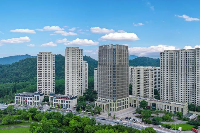 A high-rise residential building complex with multiple apartment buildings, surrounded by greenery and a clear sky.