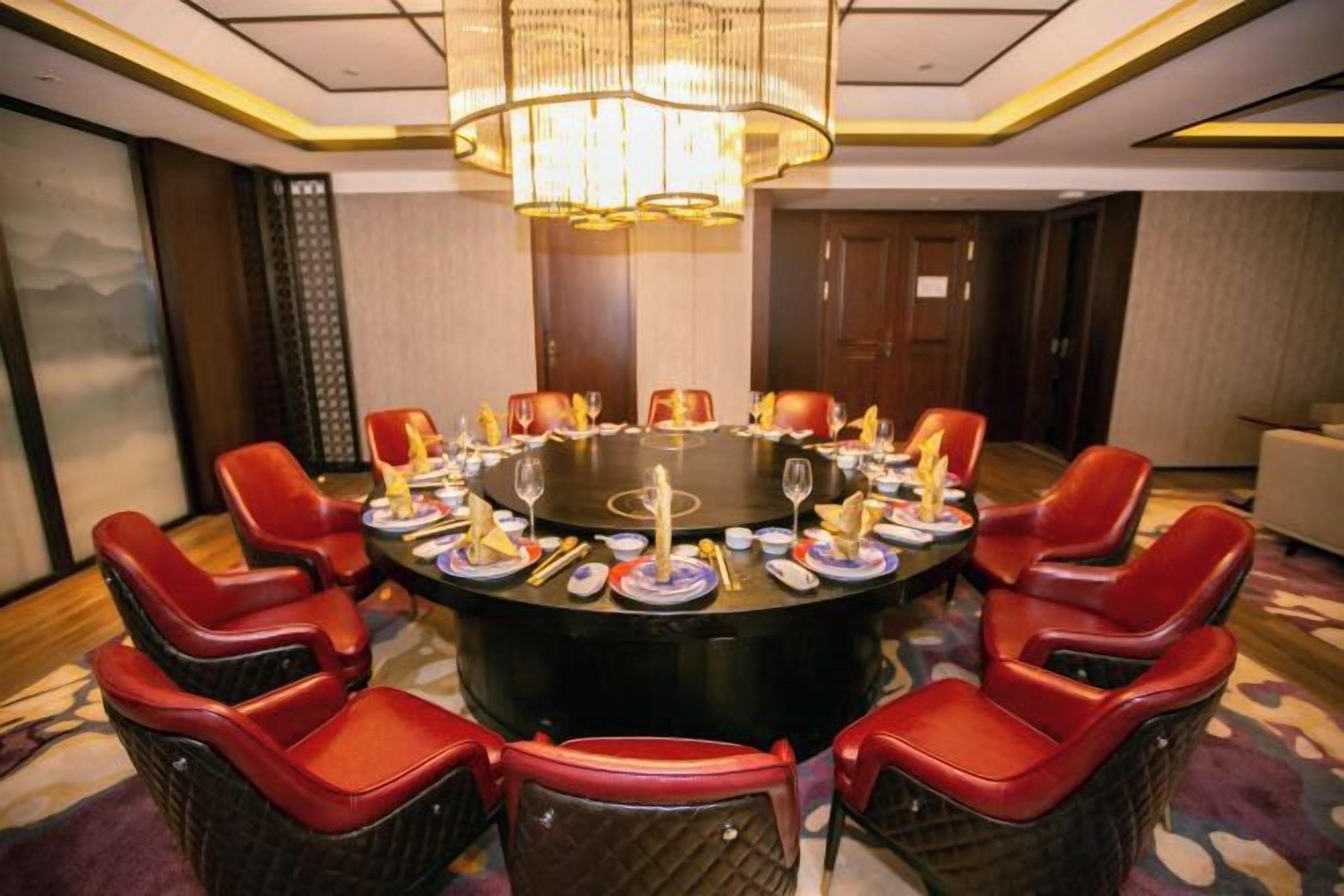 A conference room with a round table, red chairs, and a chandelier.