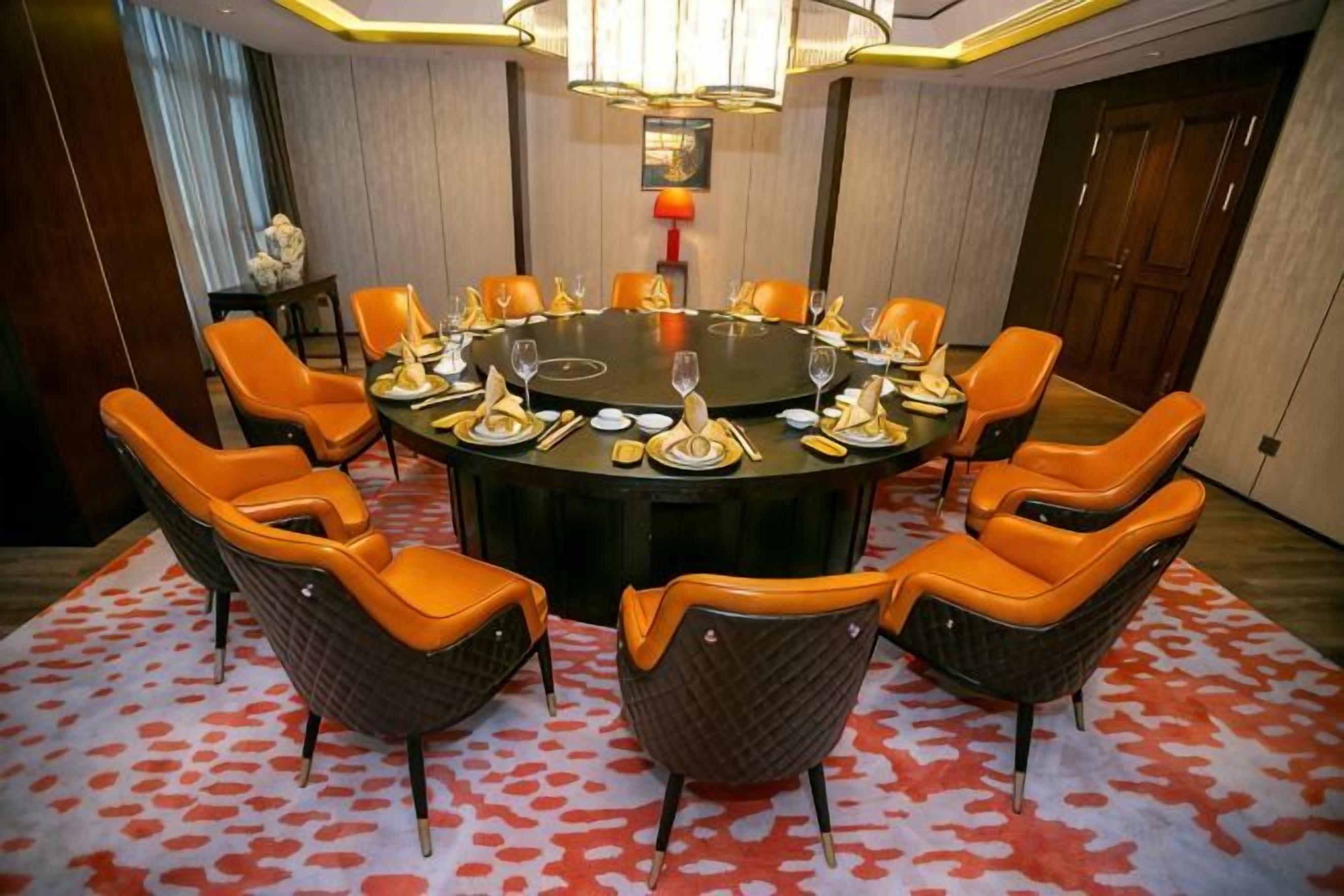 A conference room with a round table, orange chairs, and a patterned carpet.