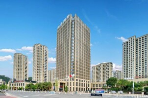 Un edificio de gran altura con un diseño arquitectónico moderno, rodeado de otros edificios altos, bajo un cielo azul despejado.