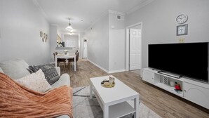 Una sala de estar moderna con sofá, mesa de centro, televisor y una zona de comedor con sillas y mesa.