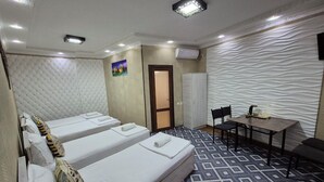 A hotel room with two single beds, a small table with chairs, a patterned floor, and a textured wall. - Vazira Hotel (Samarkand)