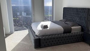 A modern bedroom with a large bed, a view of the city, and a large window. - 3Bed Apt Sleeps 6 - City Central with Wifi (Manchester)
