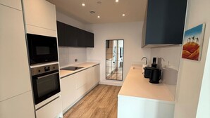 A modern kitchen with white cabinetry, a built-in oven, a microwave, and a large window. - 3Bed Apt Sleeps 6 - City Central with Wifi (Manchester)