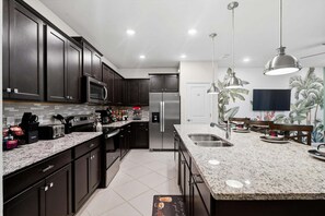 A modern kitchen with dark cabinetry, stainless steel appliances, granite countertops, and pendant lighting.