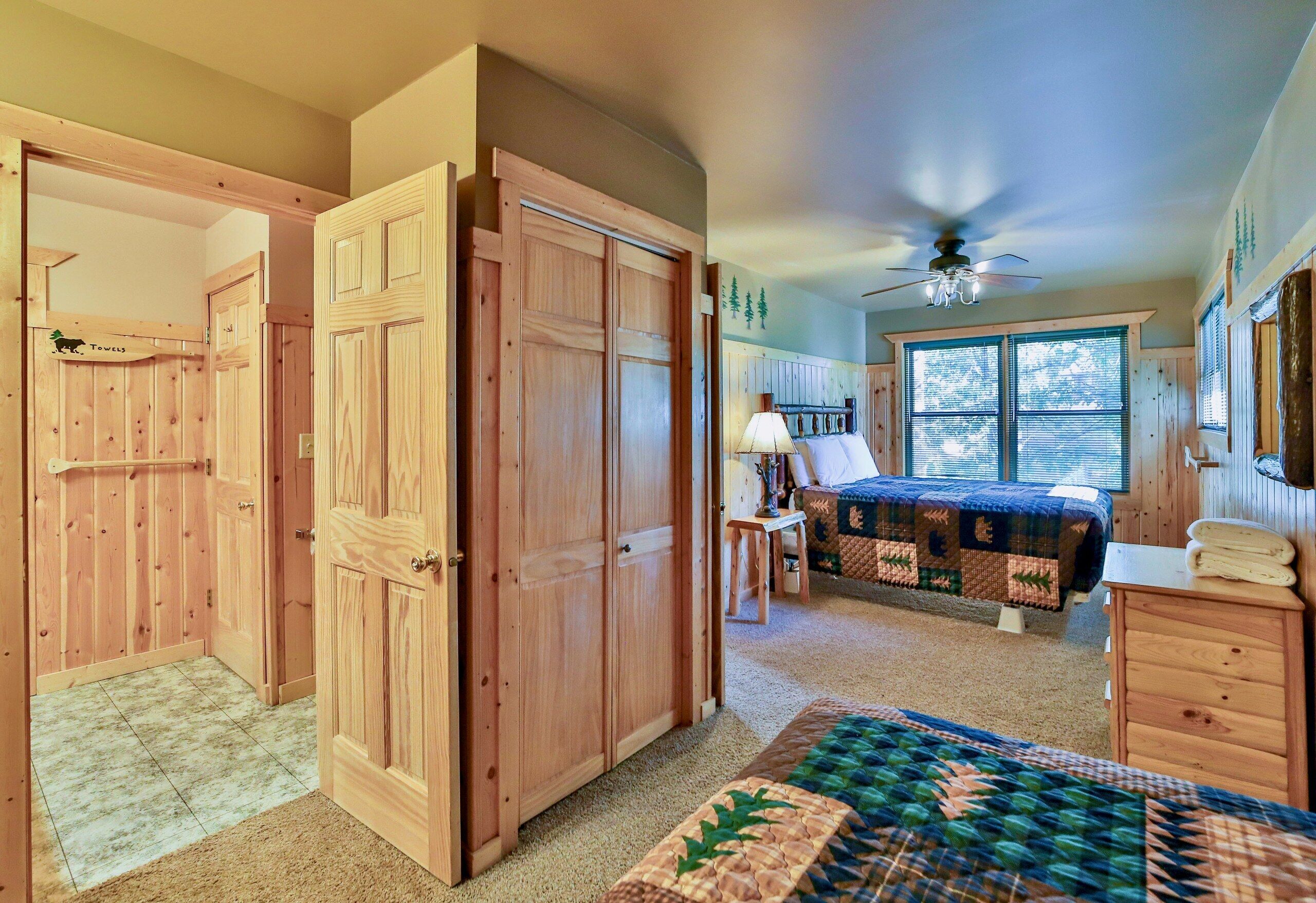 A bedroom with a bed, a desk, a chair, a ceiling fan, and wooden doors.