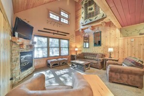 Ein gemütliches Blockhaus-Interieur mit Kamin aus Stein, Holzwänden, einer Couch und einem Fernseher.