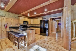 A kitchen with wooden cabinets, a stainless steel refrigerator, a bar area with stools, and a wooden floor.