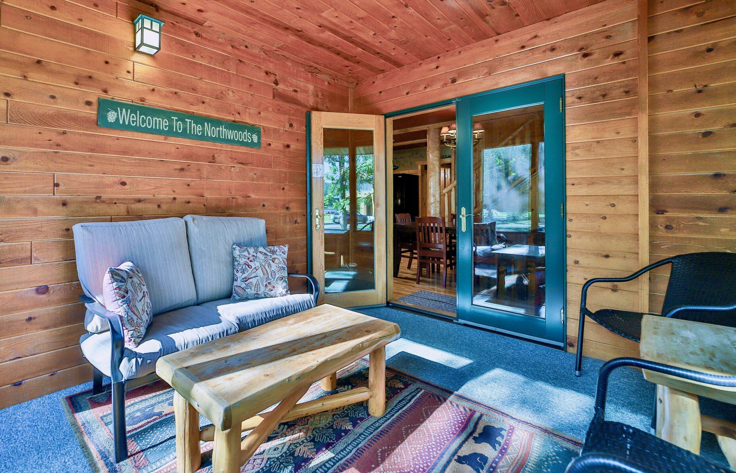 Ein Holzblockhaus-Interieur mit einer Couch, einem Tisch und einer Bank. Ein Schild trägt die Aufschrift 'Welcome To The Northwoods'.