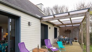 An outdoor patio with wooden deck, covered seating area, and a table with chairs. - Le Nid Marin by Interhome (Kerlouan)