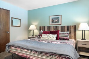 A neatly made bed with patterned bedding, a wooden headboard, bedside lamps, and a framed picture on the wall. - New! Lake Access, Pools/Hot Tub & Ski Area Proximity (Whitefish)