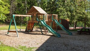 A wooden play structure with slides and swings in a park. - New! Lake Access, Pools/Hot Tub & Ski Area Proximity (Whitefish)