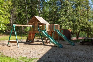 A wooden play structure with slides and swings in a park.