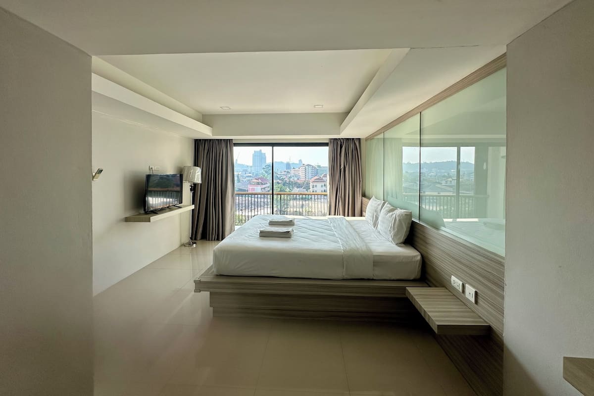 A modern hotel room with a large bed, a TV, and a city view.