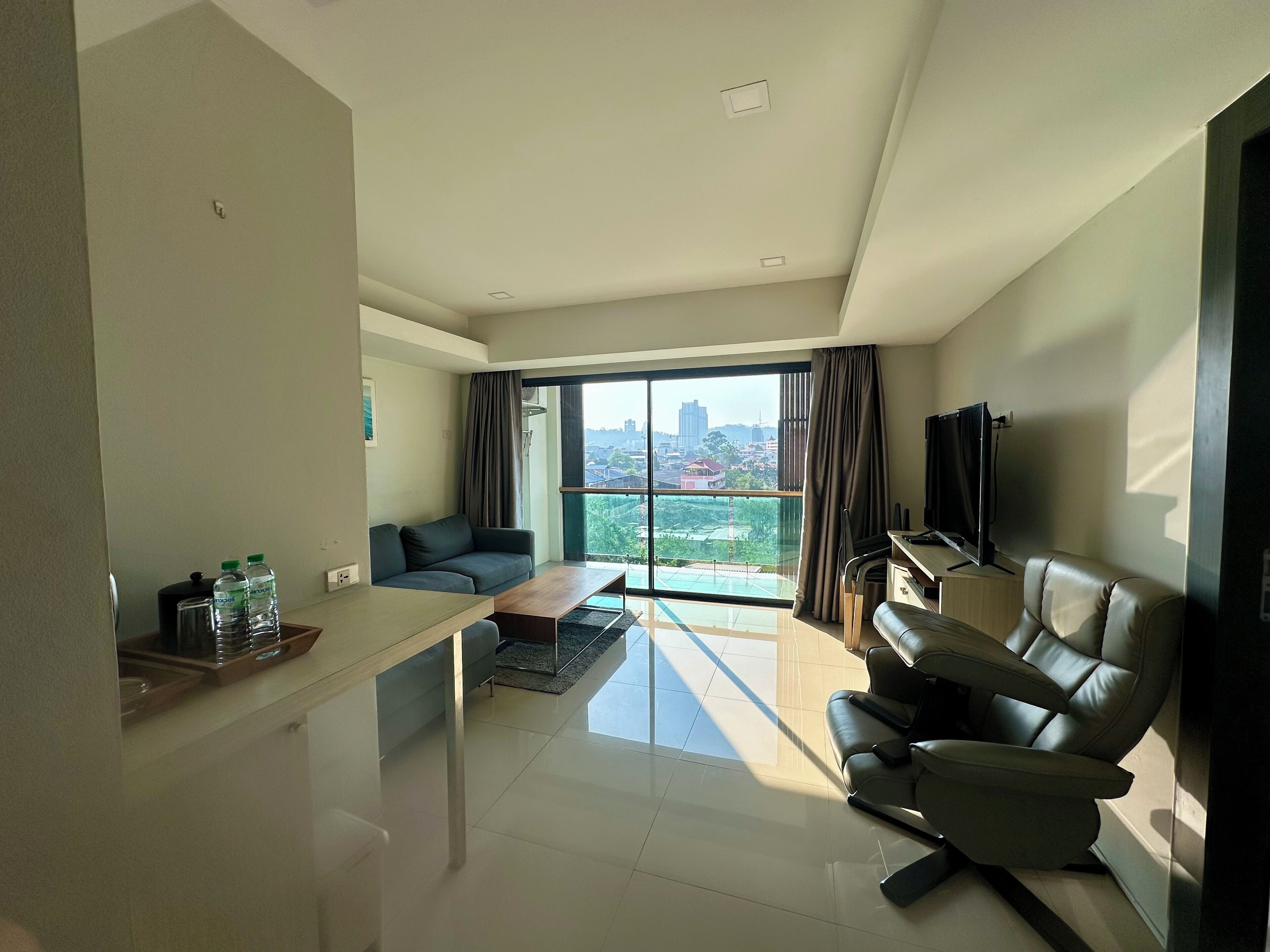 Uma sala de estar moderna com sofá, mesa de centro, TV e vista da cidade através de grandes janelas.