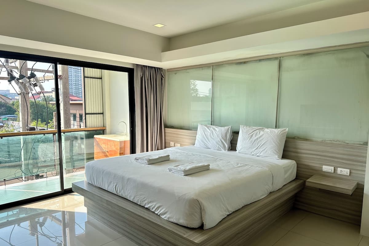A modern hotel room with a large bed, a balcony with a view, and a bathroom with a sink and mirror.