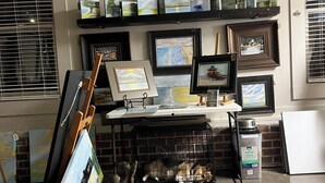 A gallery with framed artworks on shelves and a table displaying paintings.