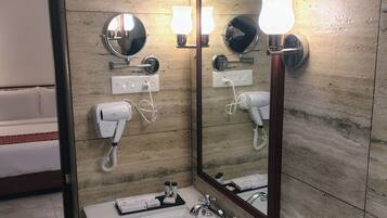 Un baño con lavamanos de mármol, un espejo grande, luces en la pared, un secador de pelo y un perchero para toallas.