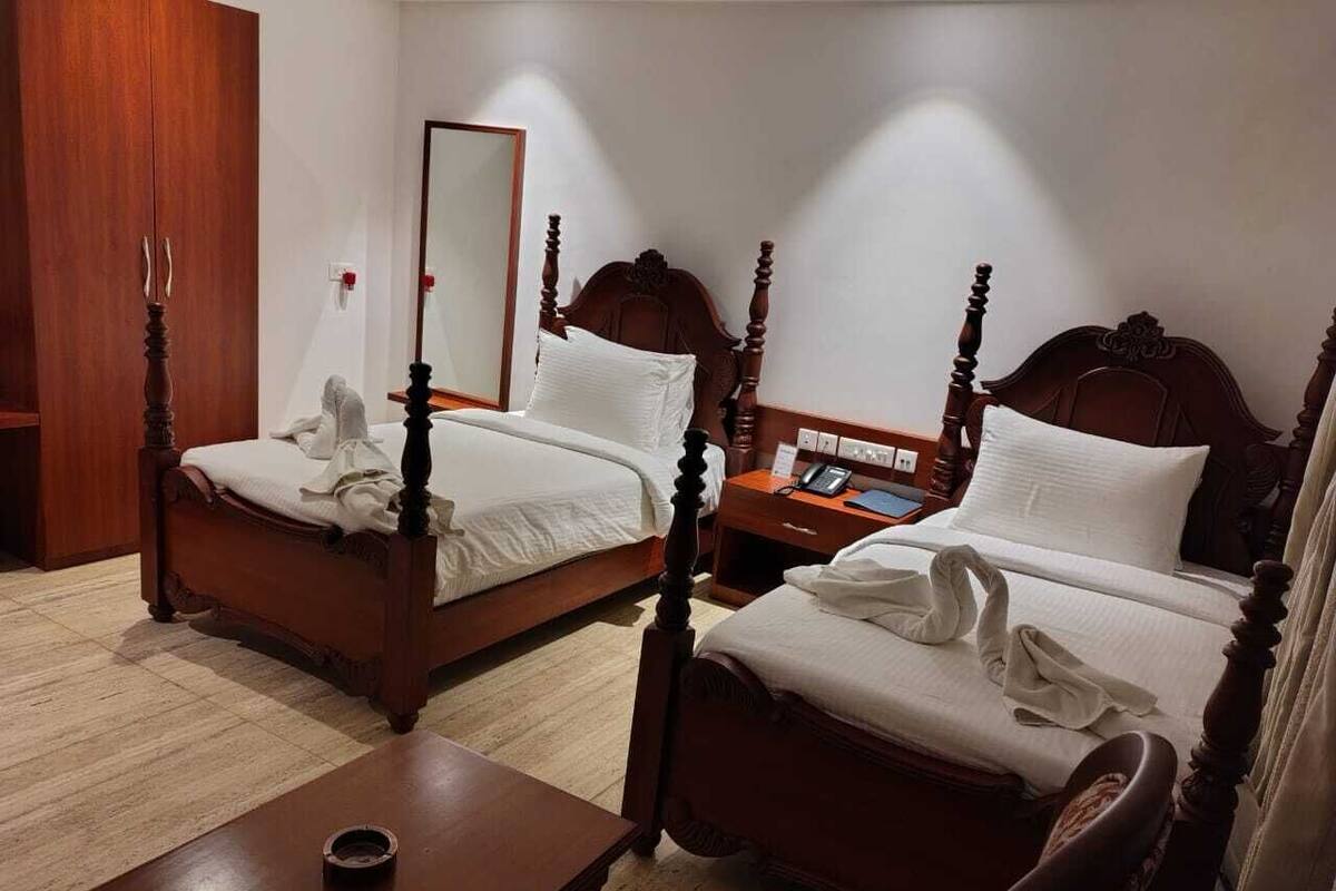 Une chambre d’hôtel avec deux lits en bois, une table de chevet, un miroir et une armoire.