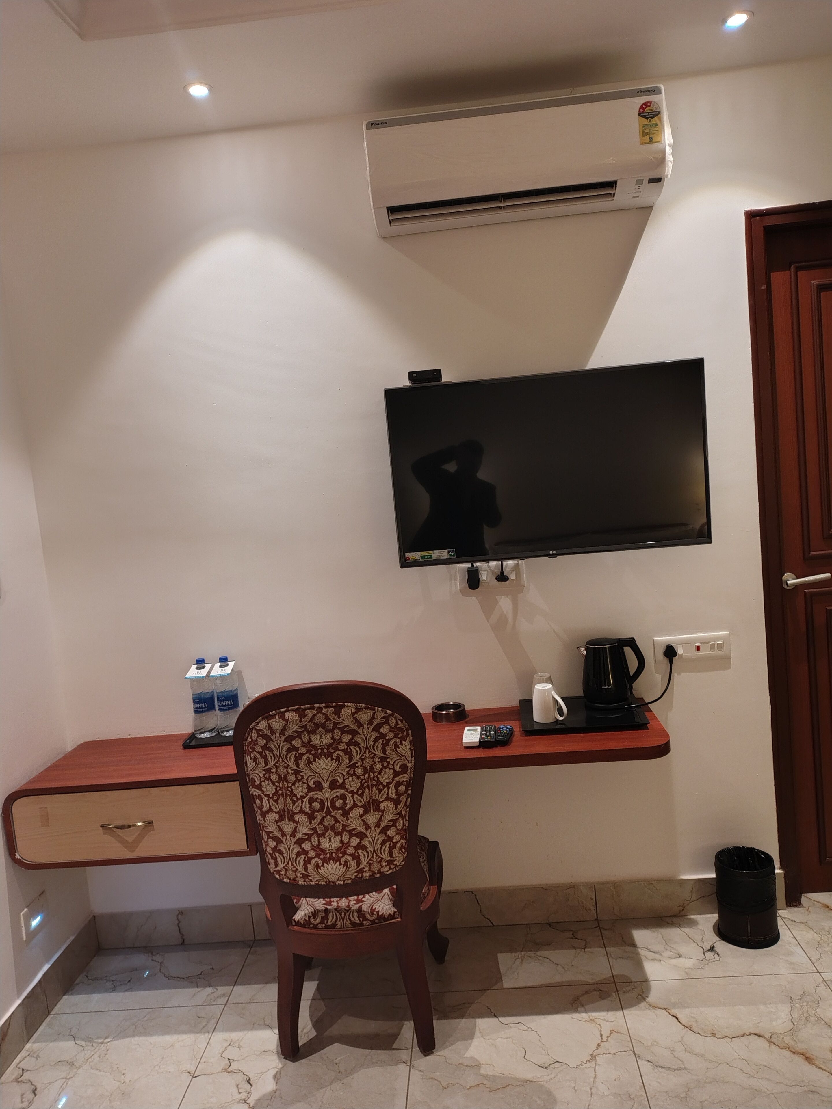 A hotel room with a desk, chair, air conditioning unit, television, and a door.