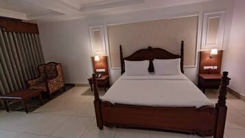 A hotel room with a large wooden bed, two bedside tables with lamps, a wooden chair, and a large window with curtains.