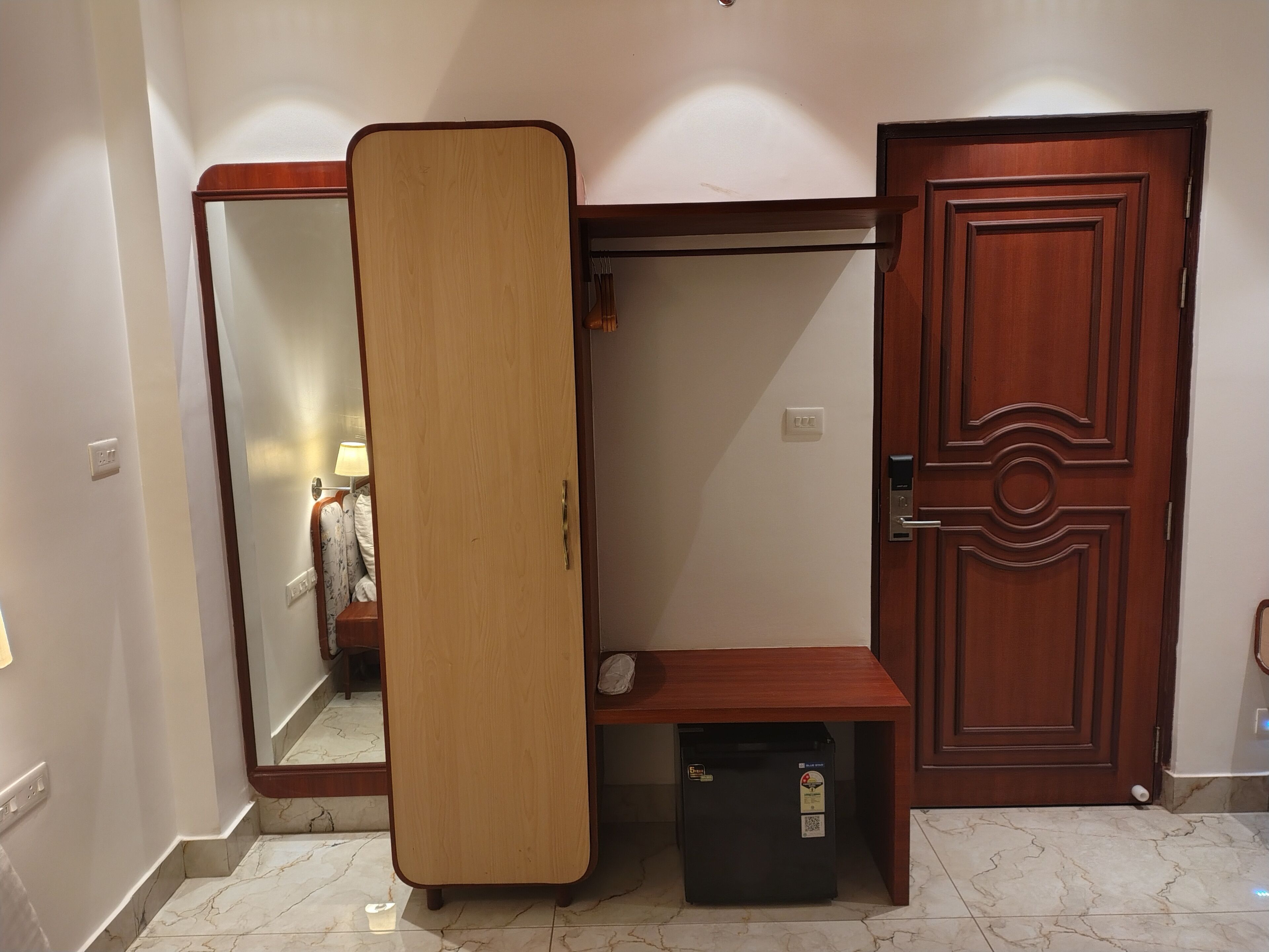 A room with a wooden wardrobe, a mirror, a small table, and a door.