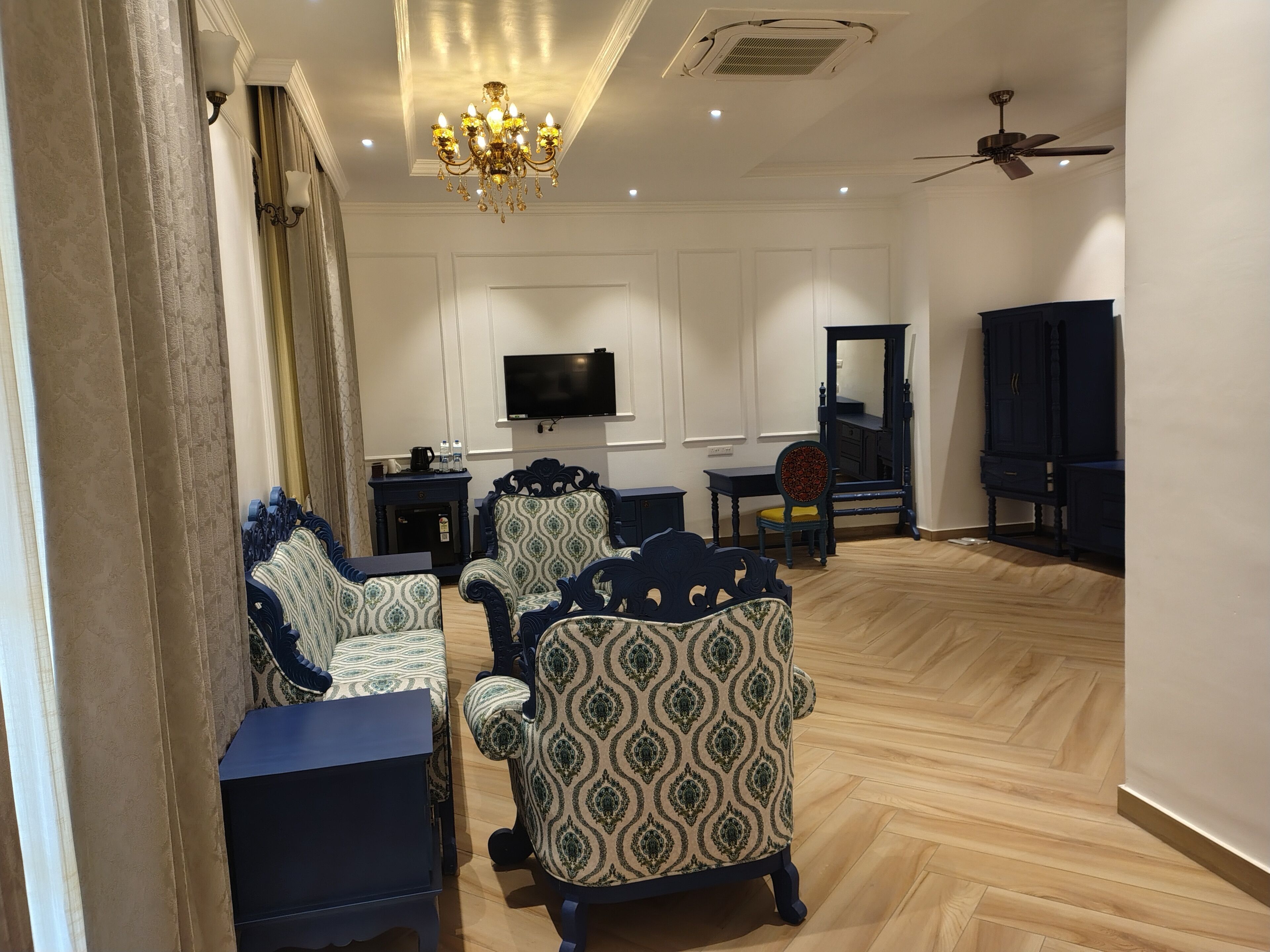 A spacious living room with patterned armchairs, a flat-screen TV, a dark wooden cabinet, and a ceiling fan.