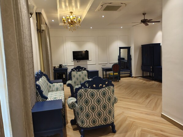A spacious living room with patterned armchairs, a flat-screen TV, a dark wooden cabinet, and a ceiling fan. - RESORT TITLI (Bolpur)