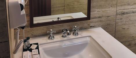 A bathroom with a large mirror, two wall-mounted lights, a hairdryer, and toiletries on the sink.