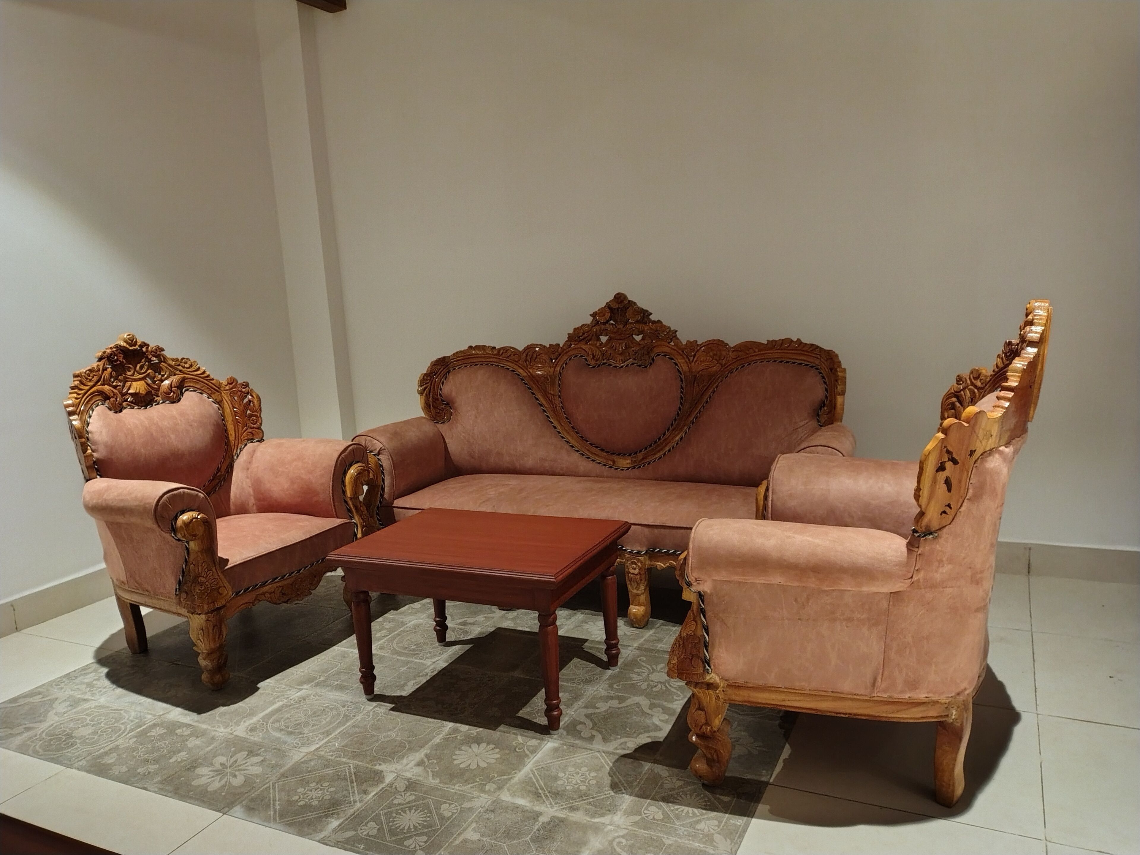 A traditional sofa set with ornate wooden armrests and legs, a matching armchair, and a small wooden coffee table.