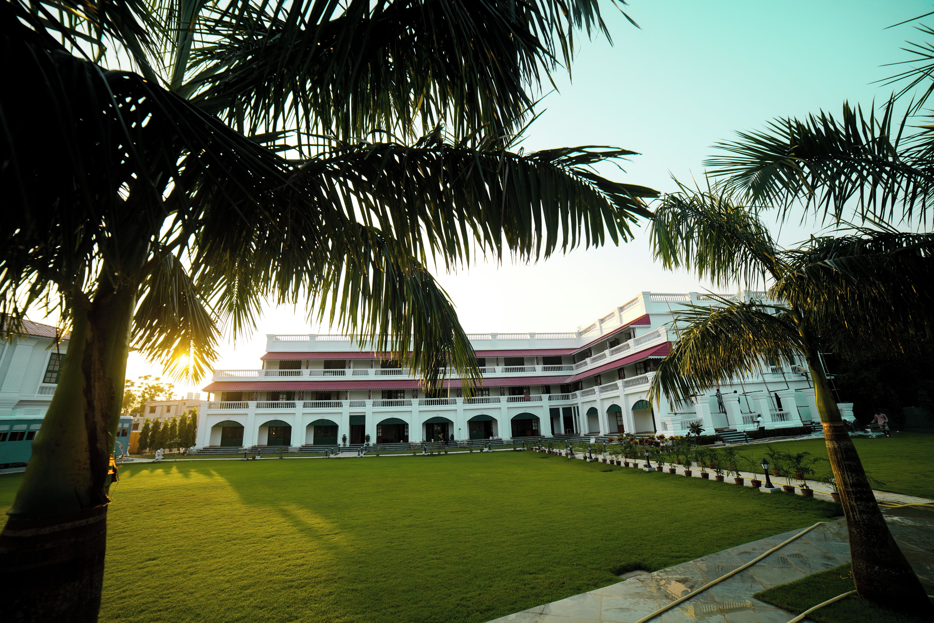 A large, multi-story building with a central courtyard, surrounded by palm trees and a well-maintained lawn.