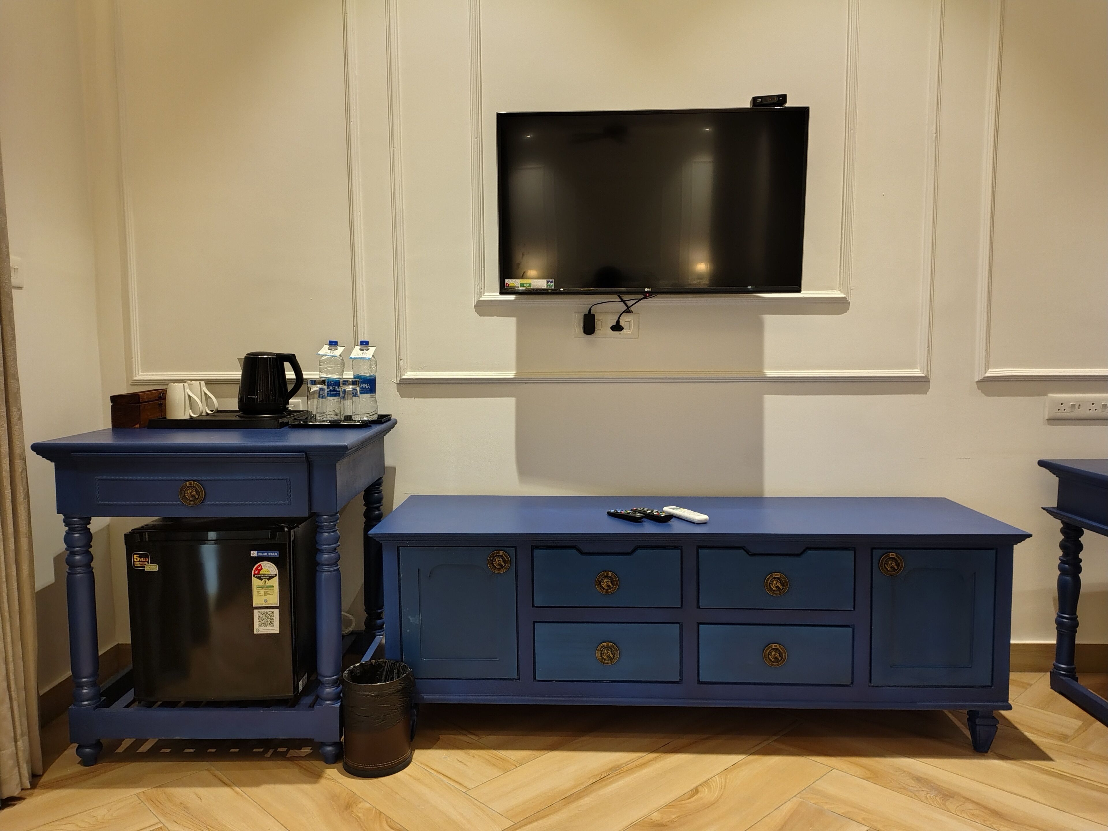 A room with a blue dresser, a small refrigerator, a television mounted on the wall, and a wooden floor.