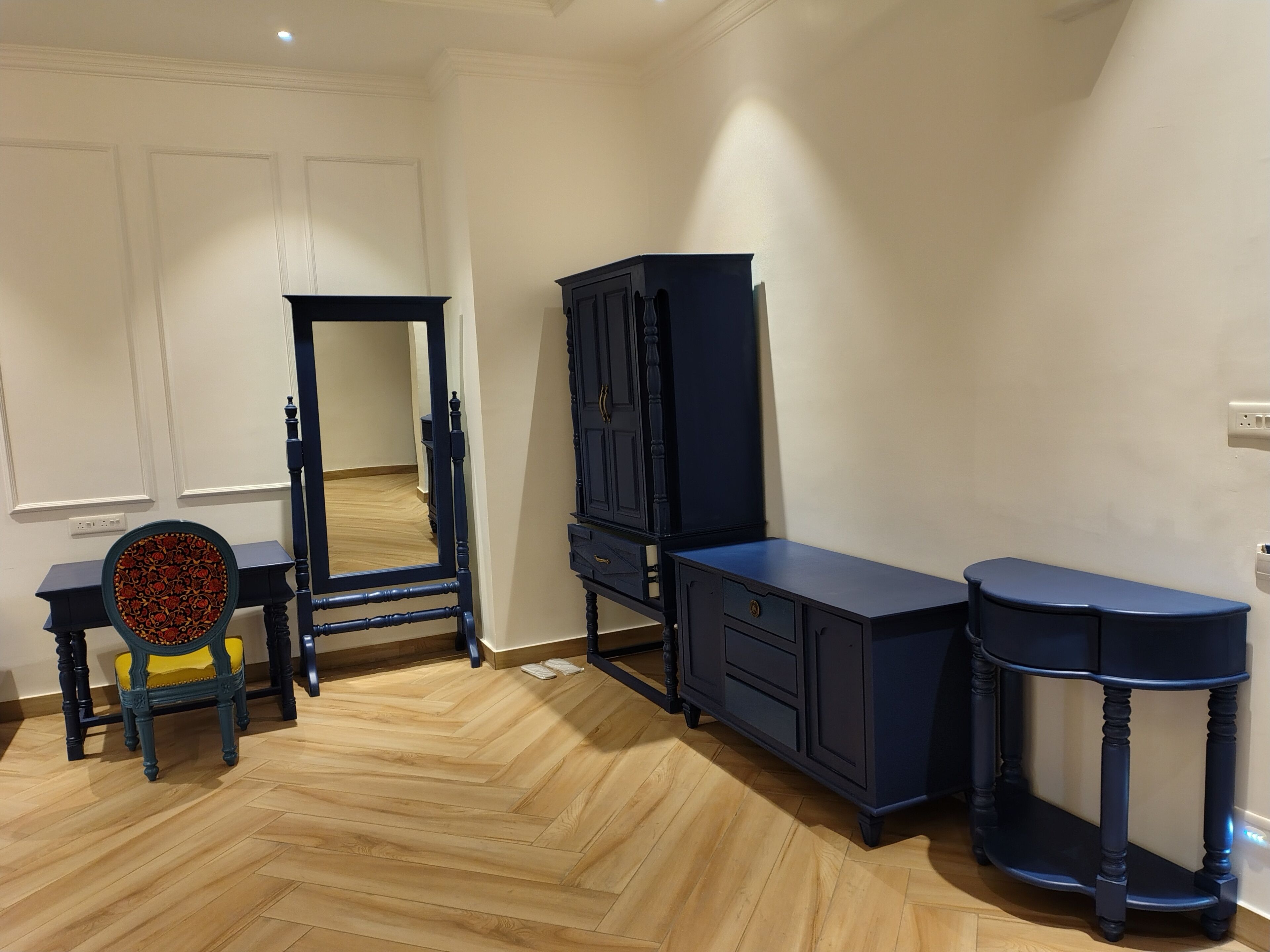 Een kamer met een visgraat parketvloer, een donkerblauwe wastafel met spiegel, een stoel met een gestreept kussen, en een donkerblauwe kast.